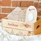 Wooden Christmas eve box with personalised Christmas gifts against a brick wall background