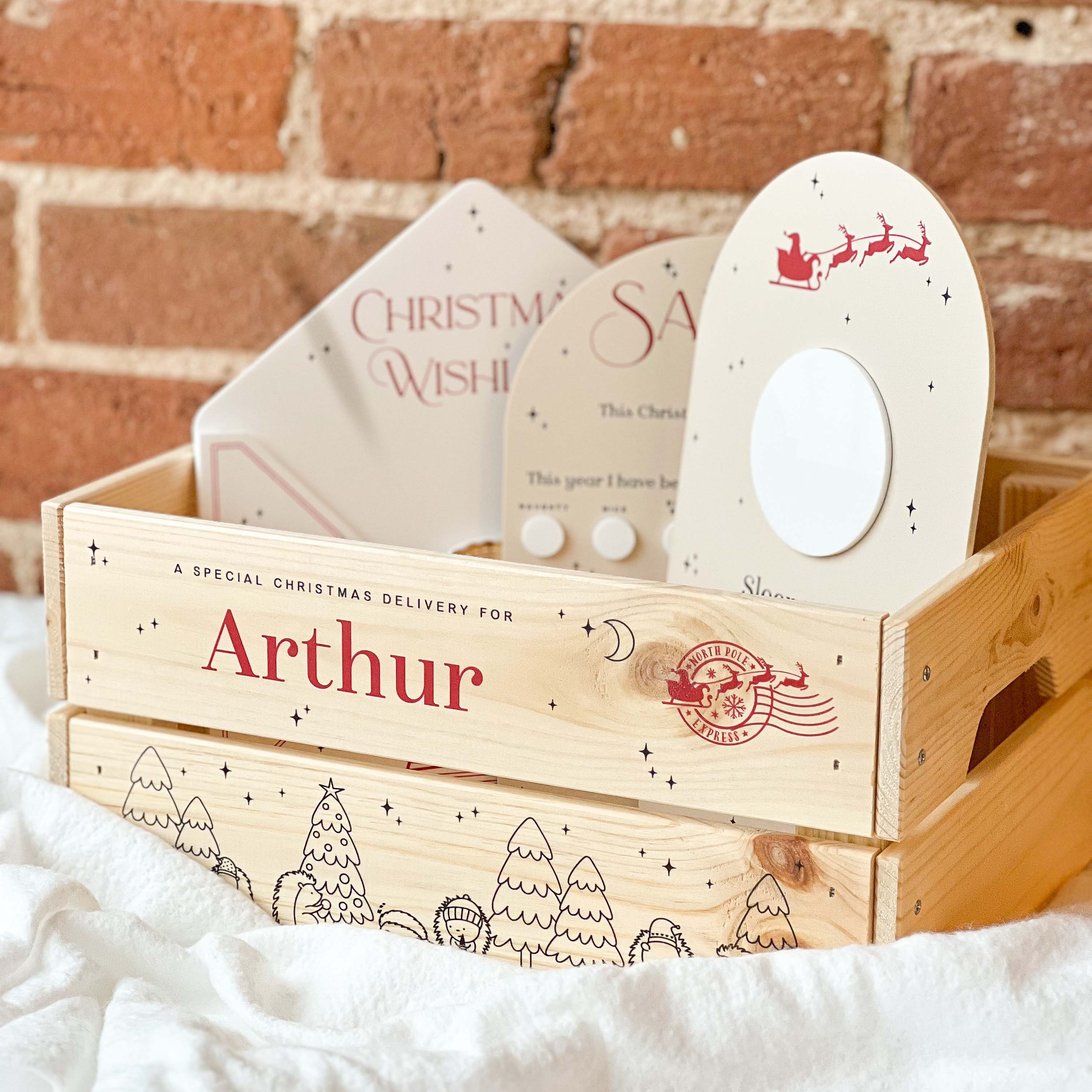 Wooden Christmas eve box with personalised Christmas gifts against a brick wall background