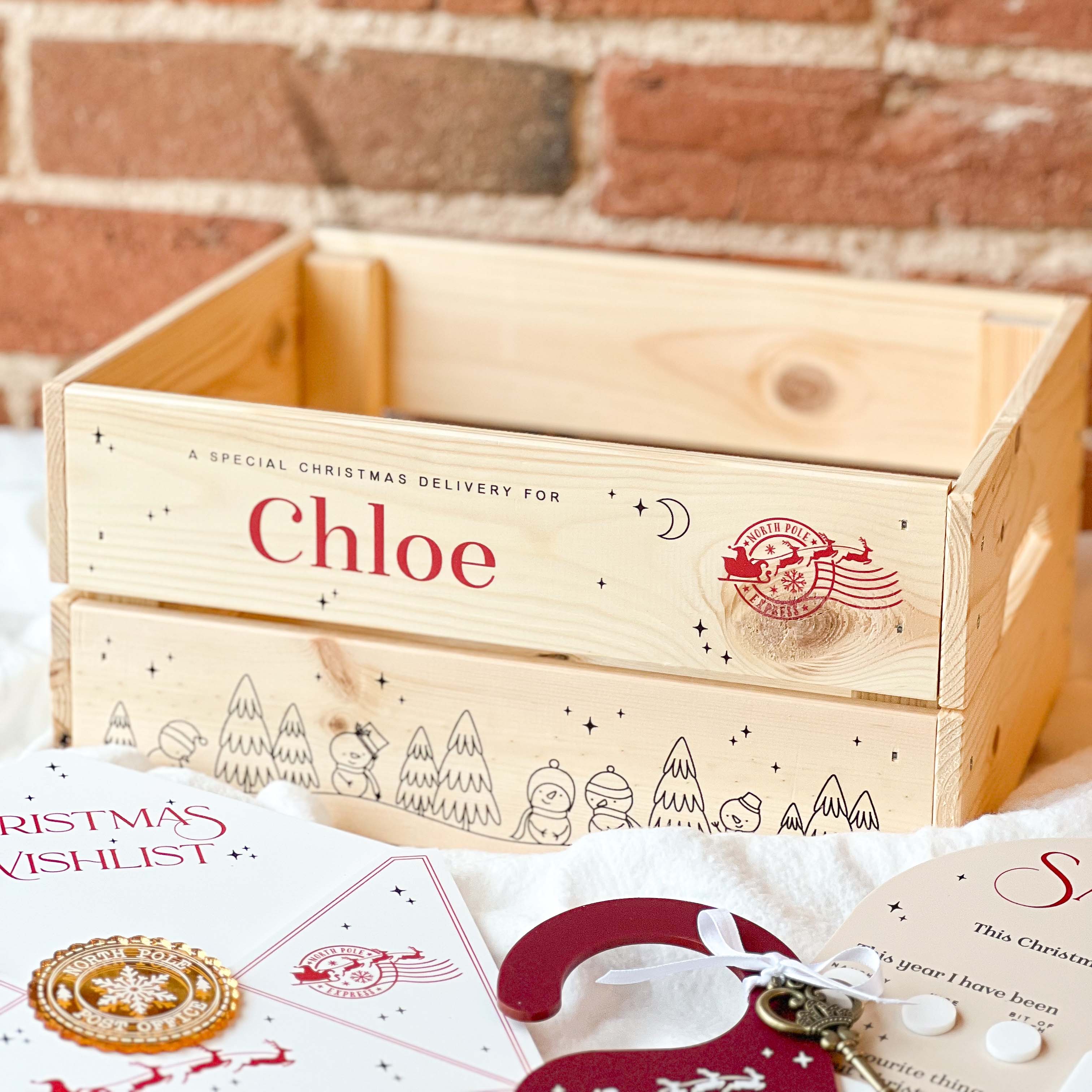Wooden Christmas Eve gift box with 'Chloe' on it, surrounded by Christmas-themed items, against a brick wall background.