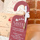 Personalised Red 'Santa's Magic Key' door hanger with a key in front of a brick background