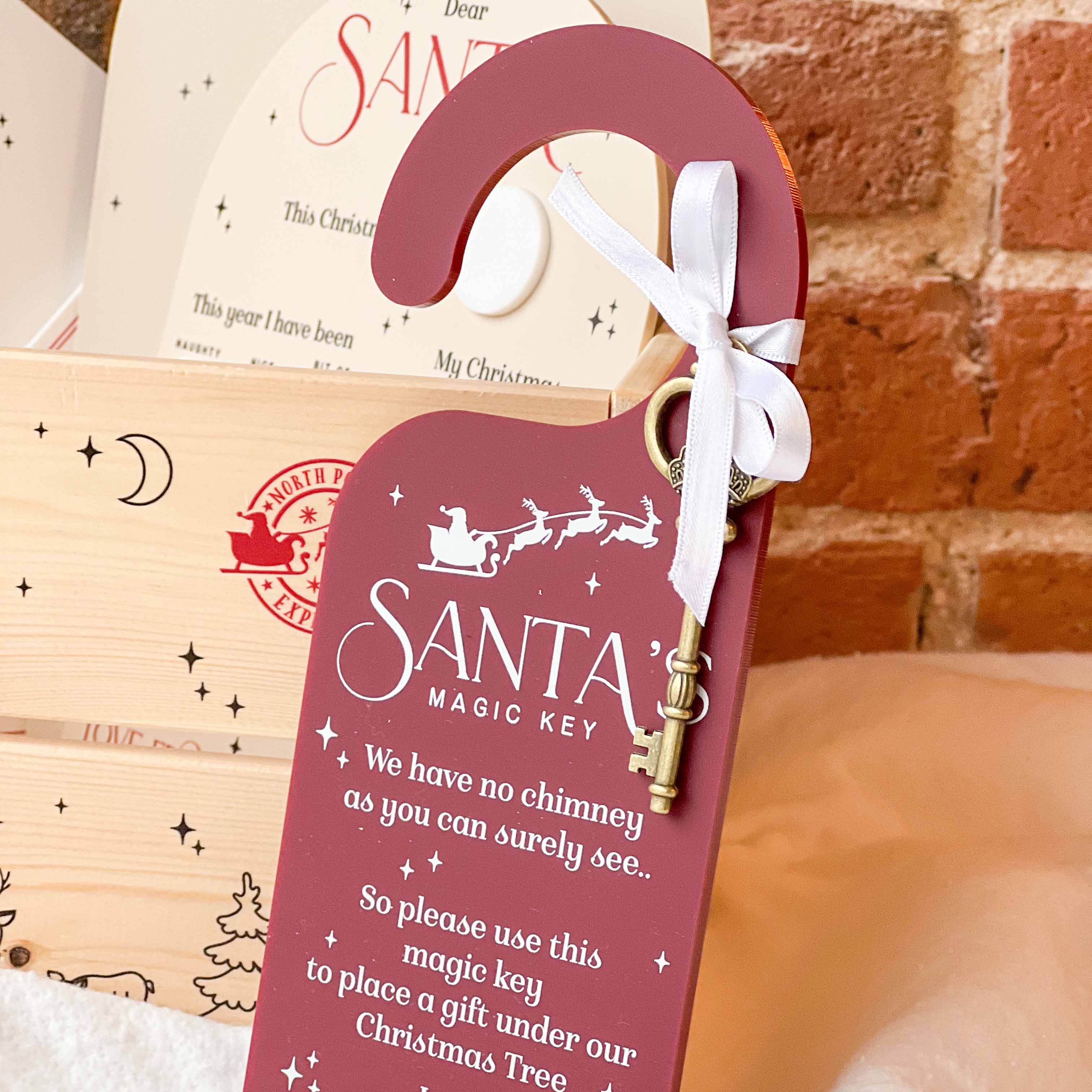 Personalised Red 'Santa's Magic Key' door hanger with a key in front of a brick background