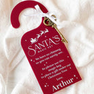 Personalised Red 'Santa's Magic Key' door hanger with a key on a white fabric background