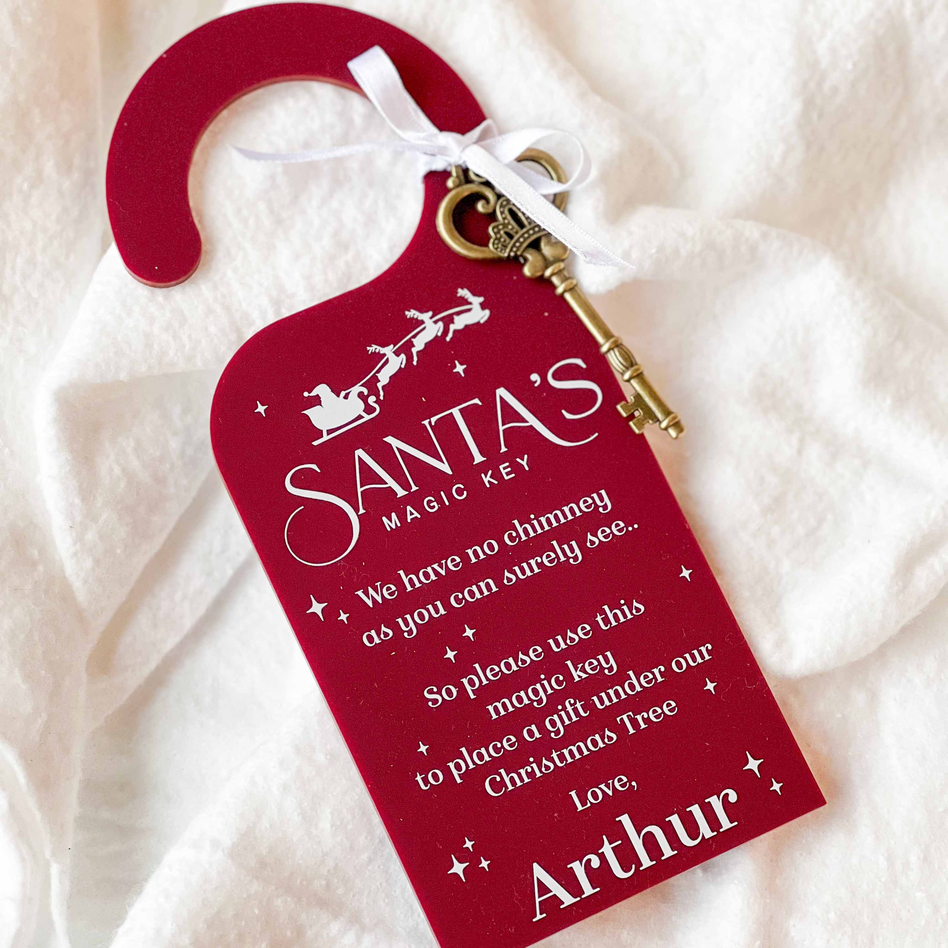 Personalised Red 'Santa's Magic Key' door hanger with a key on a white fabric background