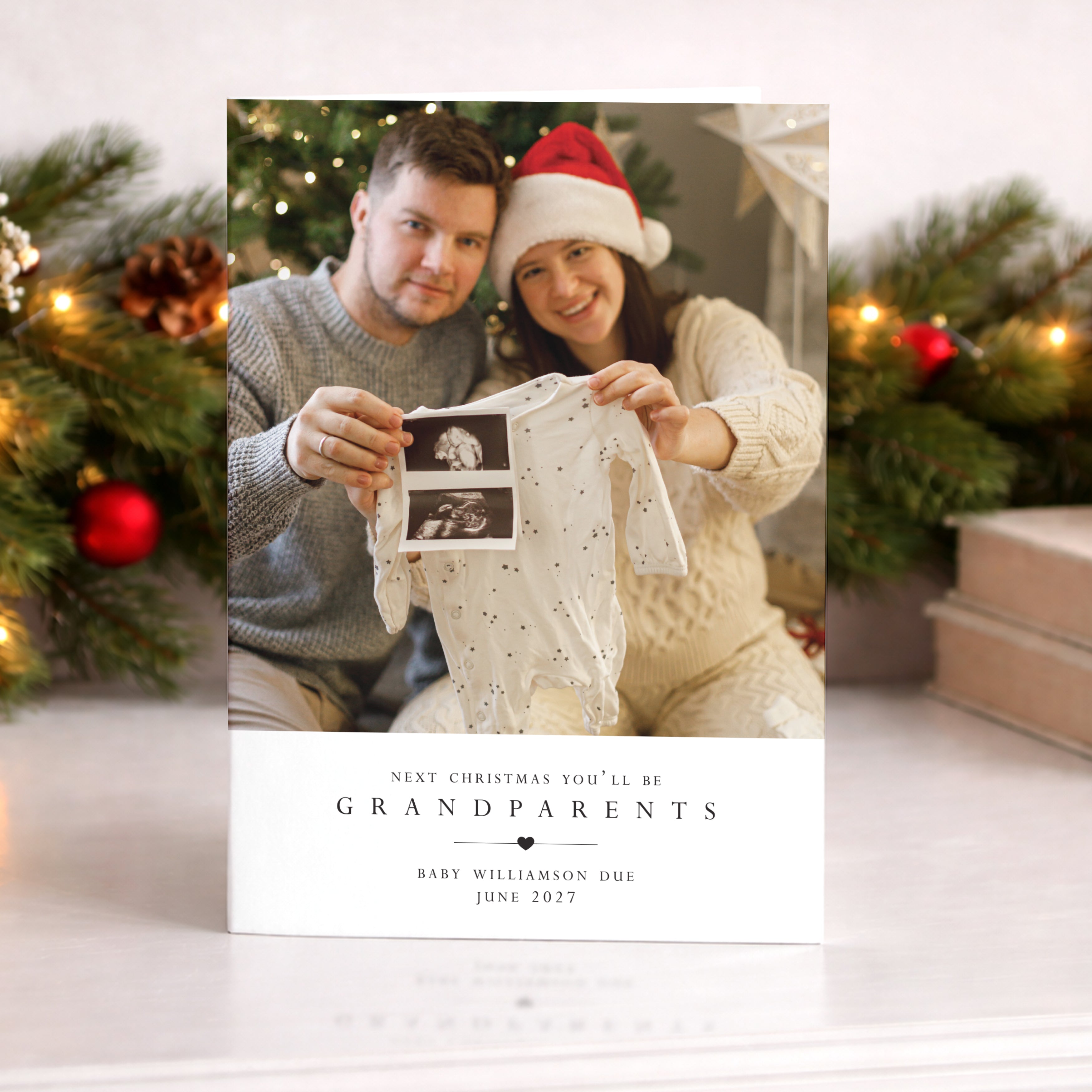 Christmas-themed pregnancy announcement card with a couple holding a baby onesie and ultrasound photo.