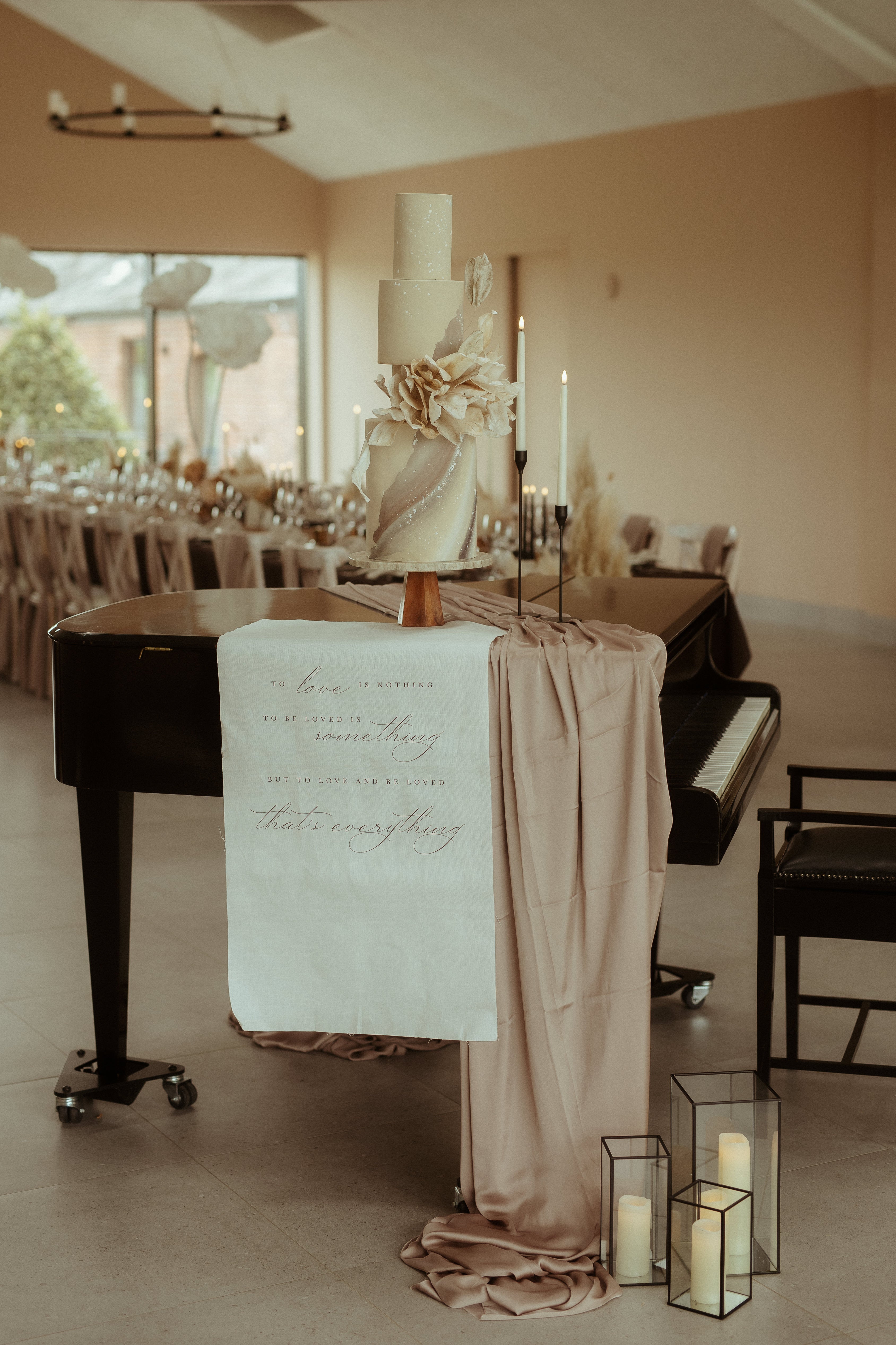 Decorated piano with a fabric sign with romantic phrase on a stand in a room with tables and chairs.