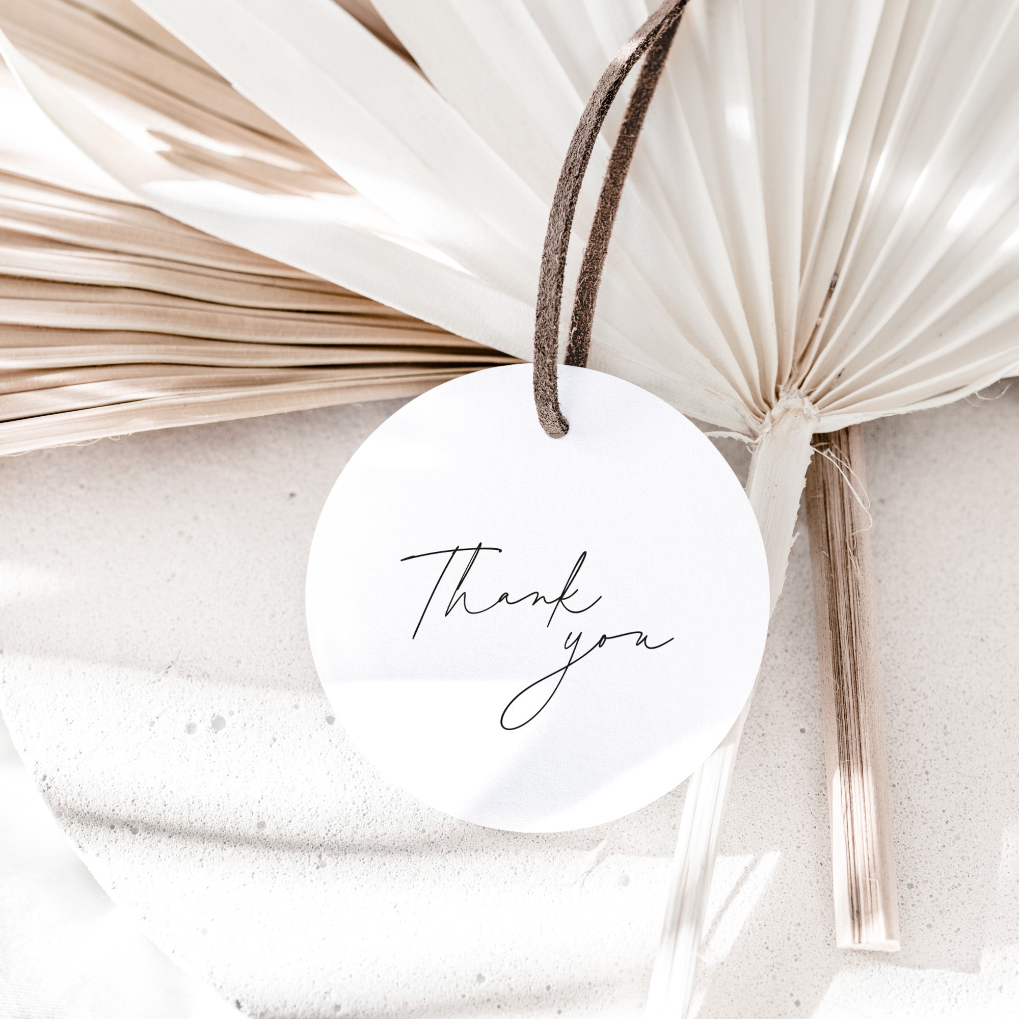 Round white tag with 'Thank You' and initials, tied with a string against a neutral background.