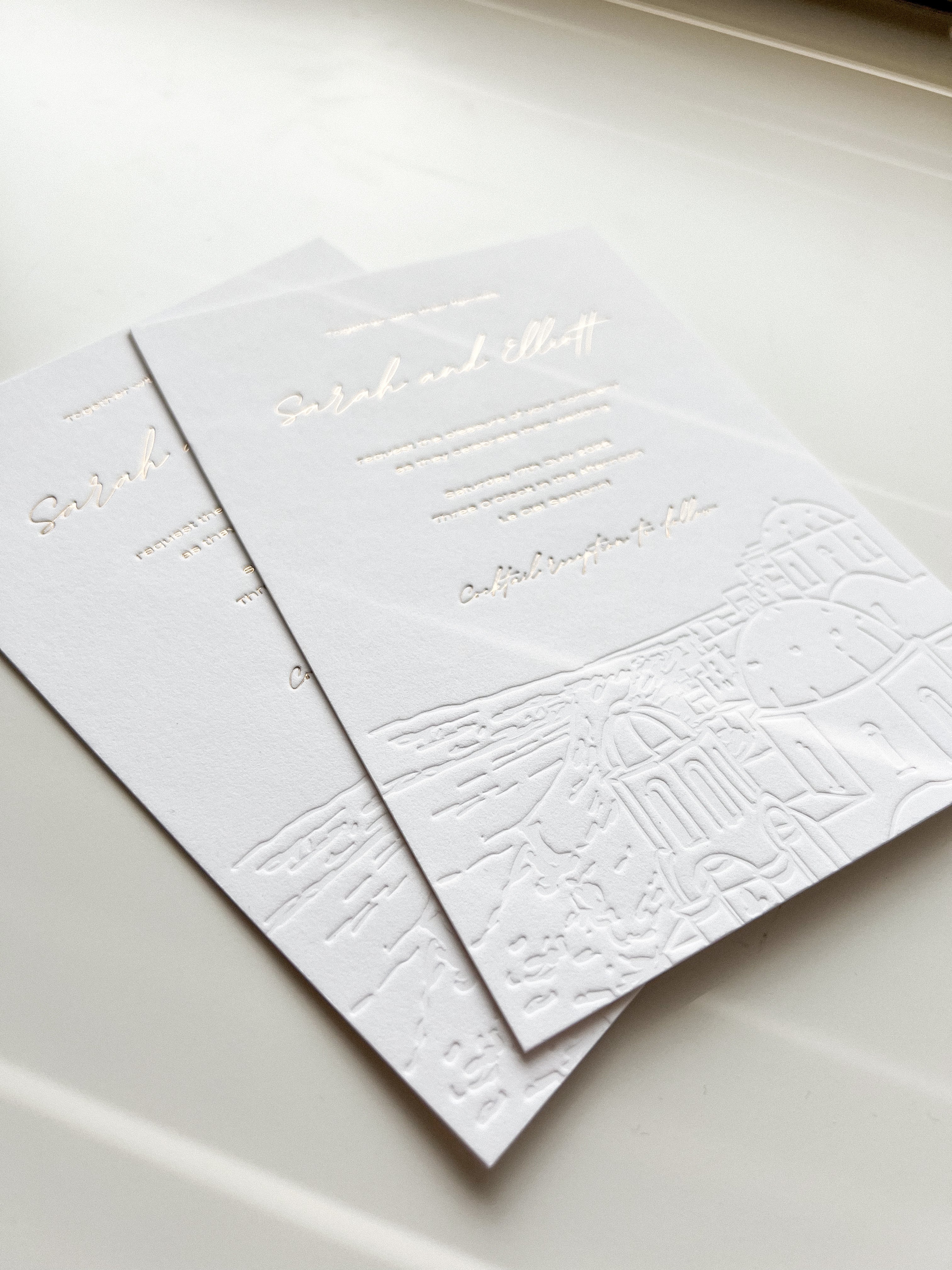Two white textured cards with gold embossed text on a light gray surface