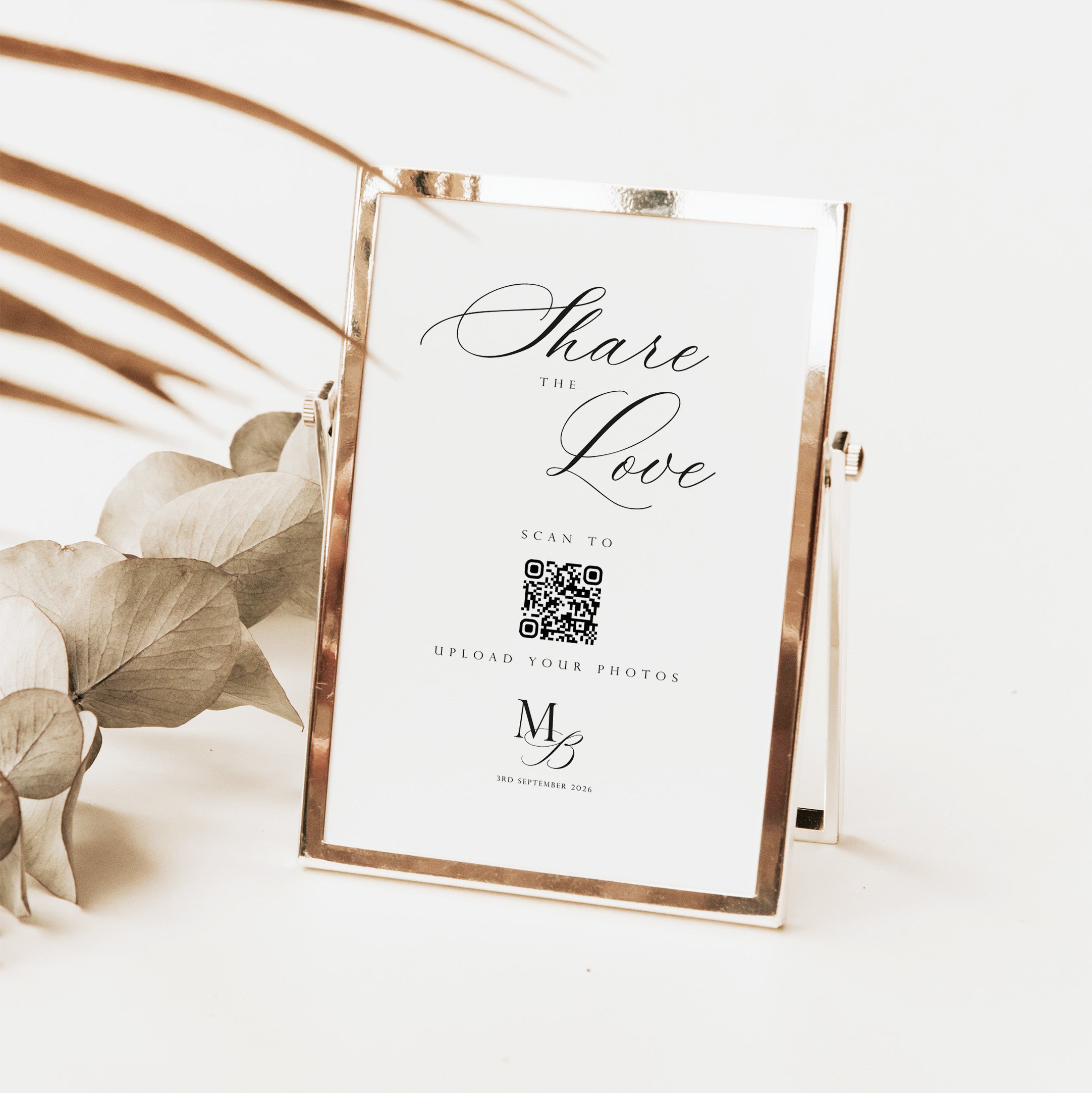 A rose gold metal picture frame with a white insert card that reads 'Share the Love' and includes a QR code, styled on a white surface with dried botanical elements.
