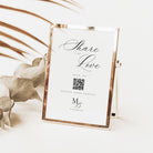A rose gold metal picture frame with a white insert card that reads 'Share the Love' and includes a QR code, styled on a white surface with dried botanical elements.