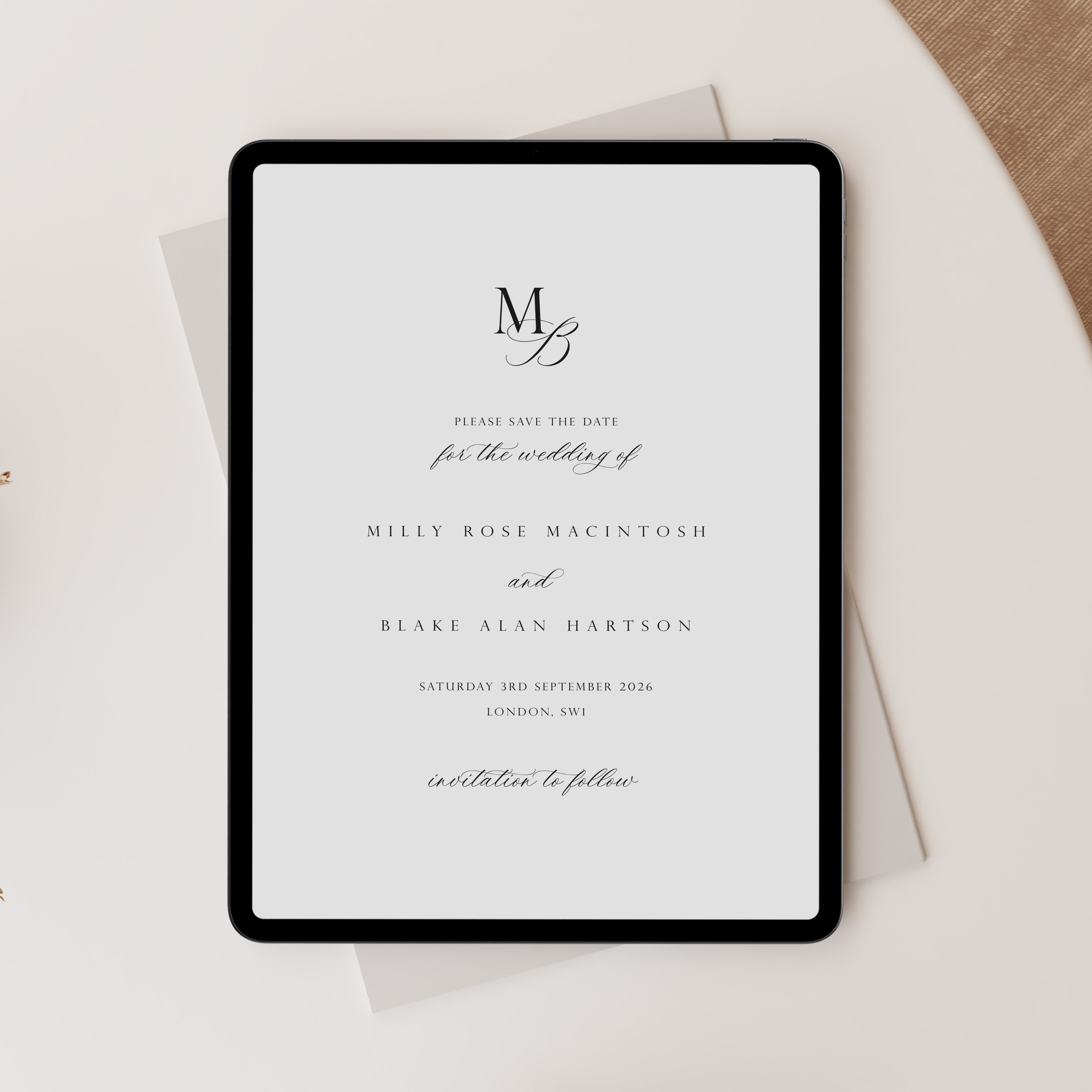 A black tablet displaying a minimalist wedding save-the-date card with elegant black typography on a white page, styled on top of a light gray envelope and a beige textured surface.