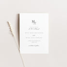 A minimalist wedding save the date card with elegant black typography on a clean white background, styled flat-lay with a dried wheat stem on a warm off-white surface.