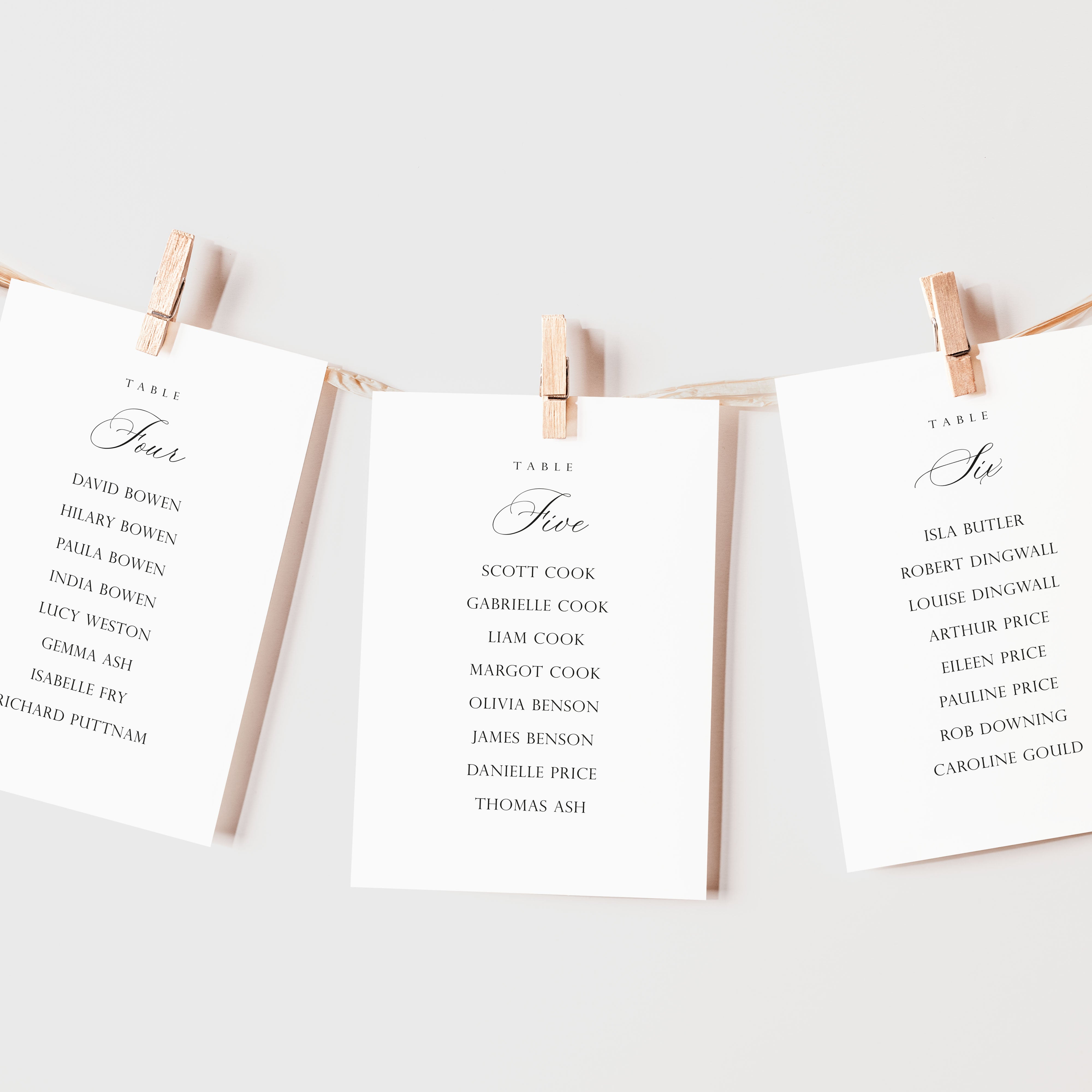 Three printed table seating cards clipped to a string with wooden clothespins against a clean white background.