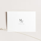 A minimalist white thank you card with a black monogram 'MB' and the words 'THANK YOU' printed in the center, styled on a light beige background with a dried wheat stem.