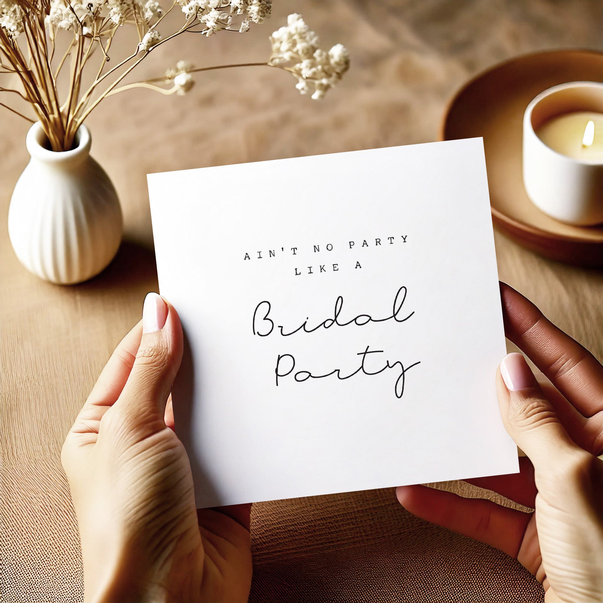 Hands holding a card with 'Ain't no party like a bridal party' text on a wooden surface with a vase and candle.
