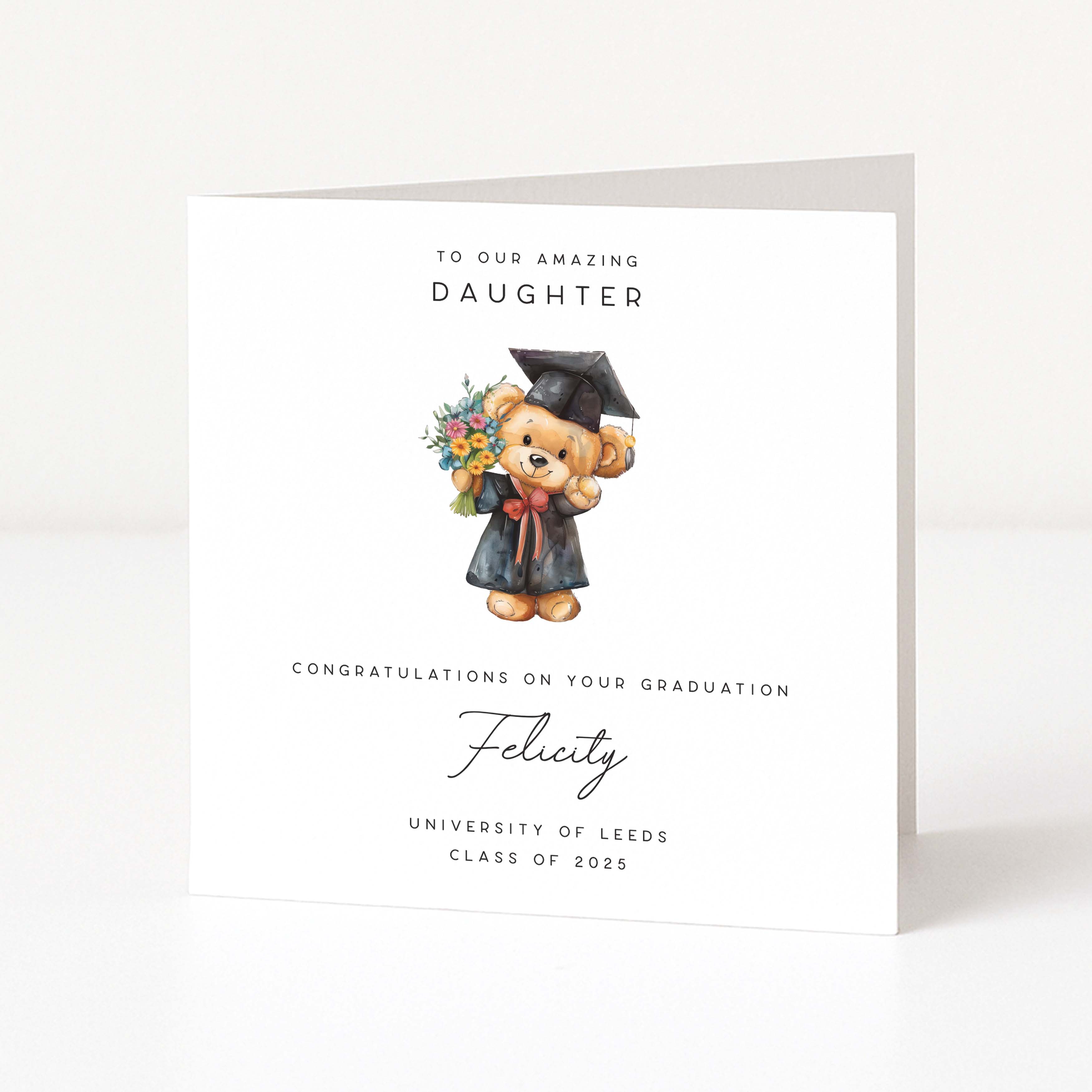 Graduation card with a teddy bear holding flowers and a mortarboard hat on a white background.