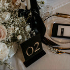 Elegant table setting with floral arrangements, candles, and black ribbons on a white tablecloth.