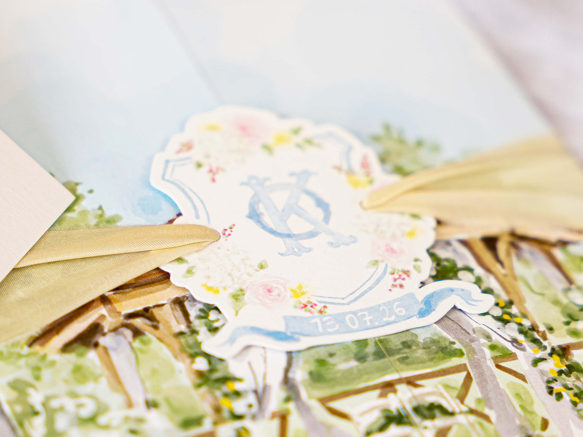 A close-up of a decorative paper cutout with a floral border, a blue monogram emblem, and the date '12.07.26'