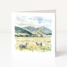 Greeting card with a scenic landscape featuring sheep in a field and mountains.