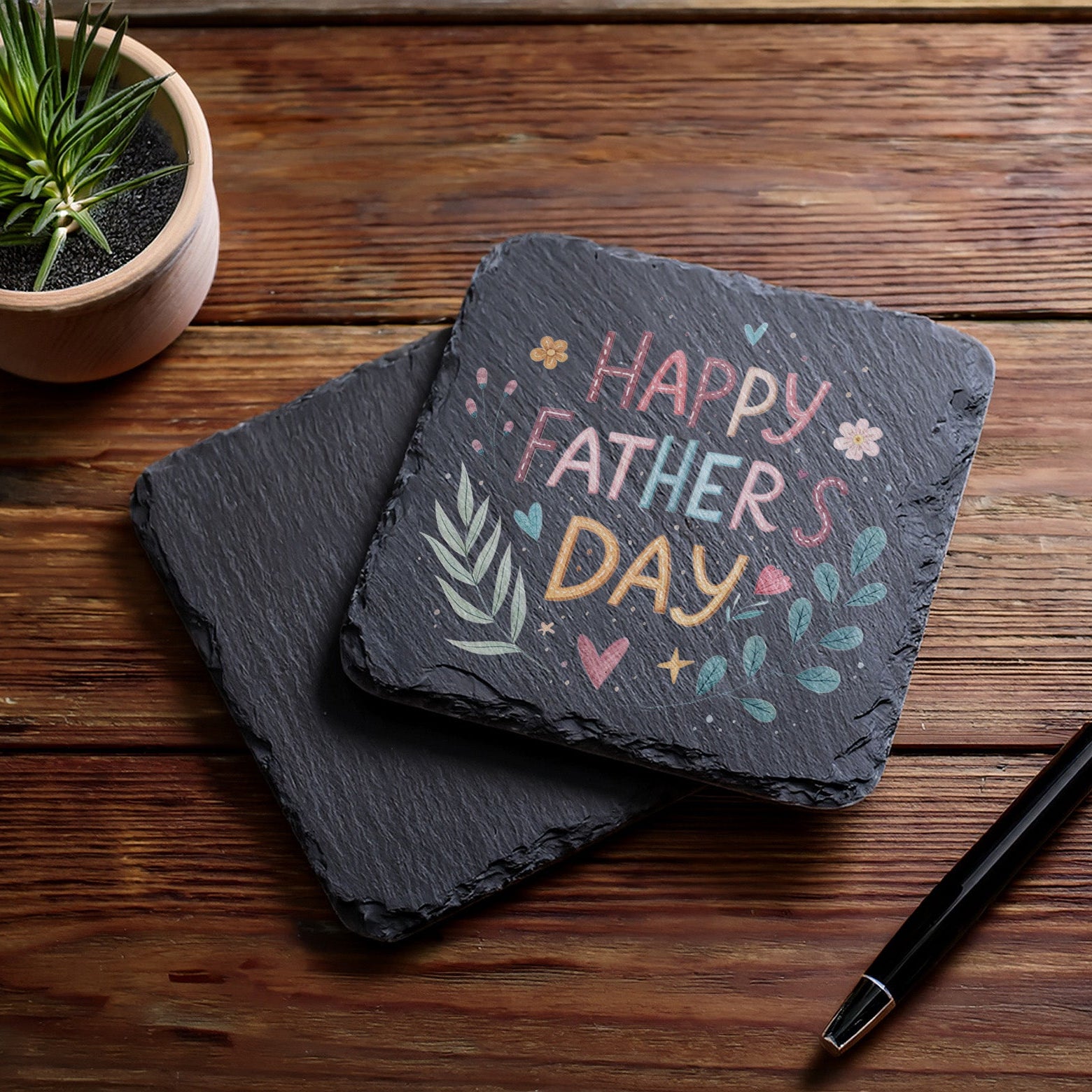 Slate with 'Happy Father's Day' text on a wooden surface with a pen and plant.