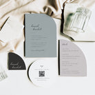 Wedding invitation set with gray and black design on a white surface with fabric and candle.
