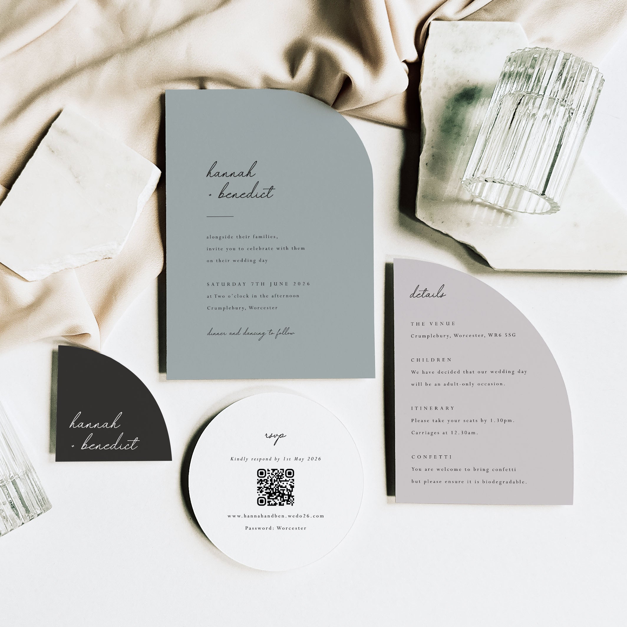 Wedding invitation set with gray and black design on a white surface with fabric and candle.