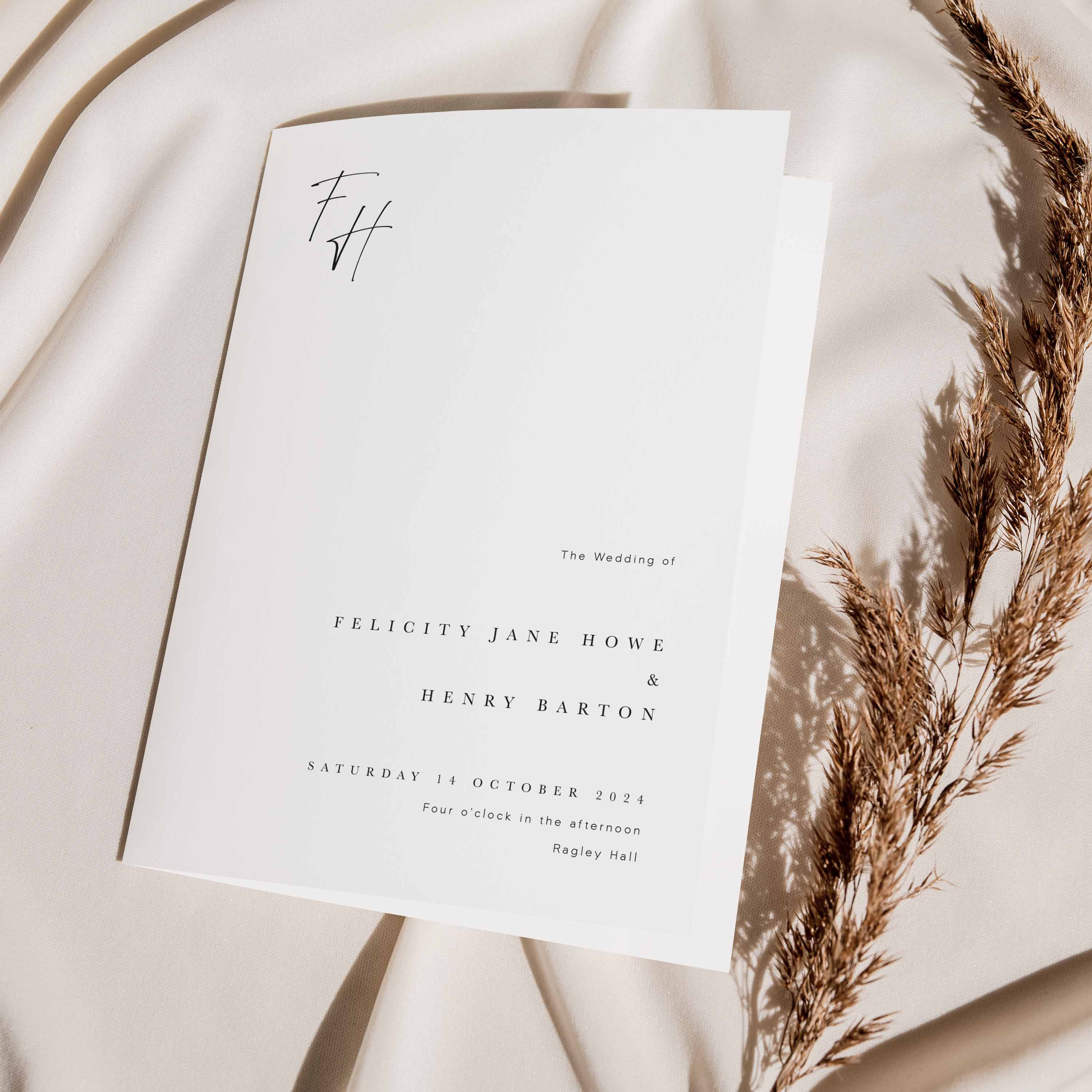 Wedding order of service booklet with dried grasses on a soft fabric background