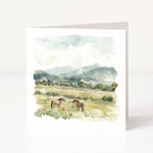 Greeting card with watercolor illustration of two horses in a field with mountains in the background.