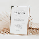 Wedding drink menu in a gold frame on a white background with dried palm leaves.
