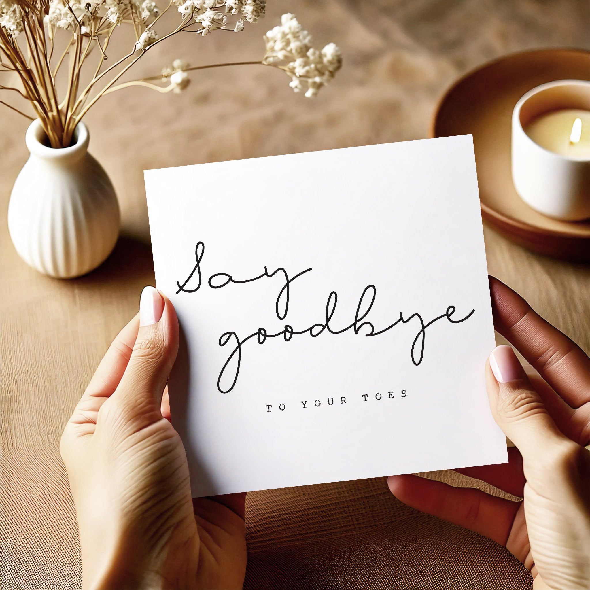 Person holding a card with 'Say goodbye to your toes' text on a wooden surface with decorative elements.