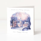 A square white greeting card standing upright, printed with a watercolor winter village scene in soft blue, purple, pink, and beige tones. The top reads 'Wishing you a Merry Christmas' and the bottom reads 'And a Happy New Year'.
