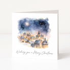 A square white greeting card standing upright, featuring a watercolor illustration of a snowy village under a starry night sky, with the text 'Wishing you a Merry Christmas' printed below.