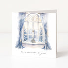 A square greeting card with a watercolor illustration of a snowy window scene, featuring blue curtains, snow-covered trees, and the text 'FROM OUR HOME to yours' at the bottom, shown standing against a white background.