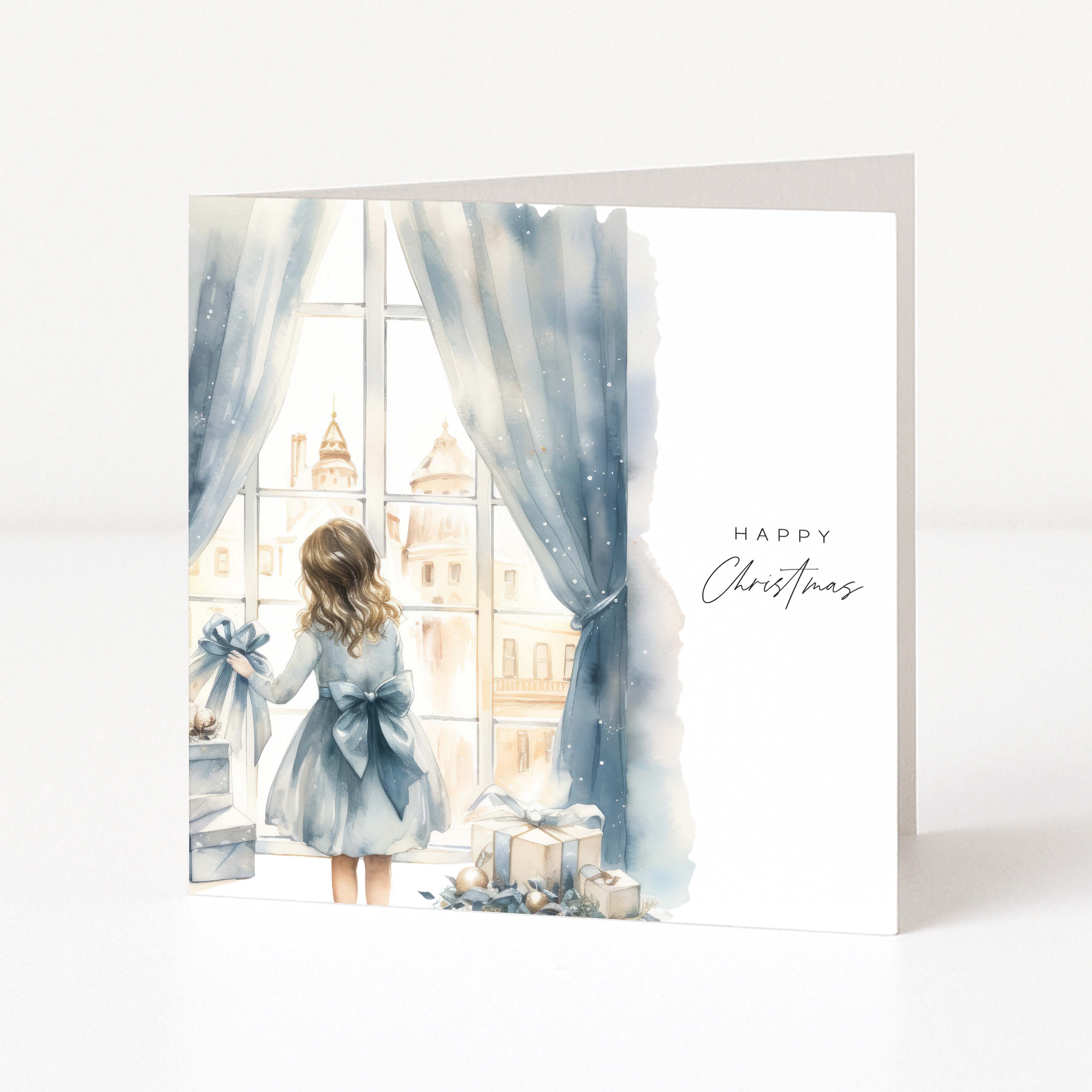 A square Christmas greeting card with a watercolor illustration of a young girl in a blue dress standing by a window with blue curtains, looking out at buildings, with wrapped gifts on the floor. The right side of the card has 'Happy Christmas' printed in black script.