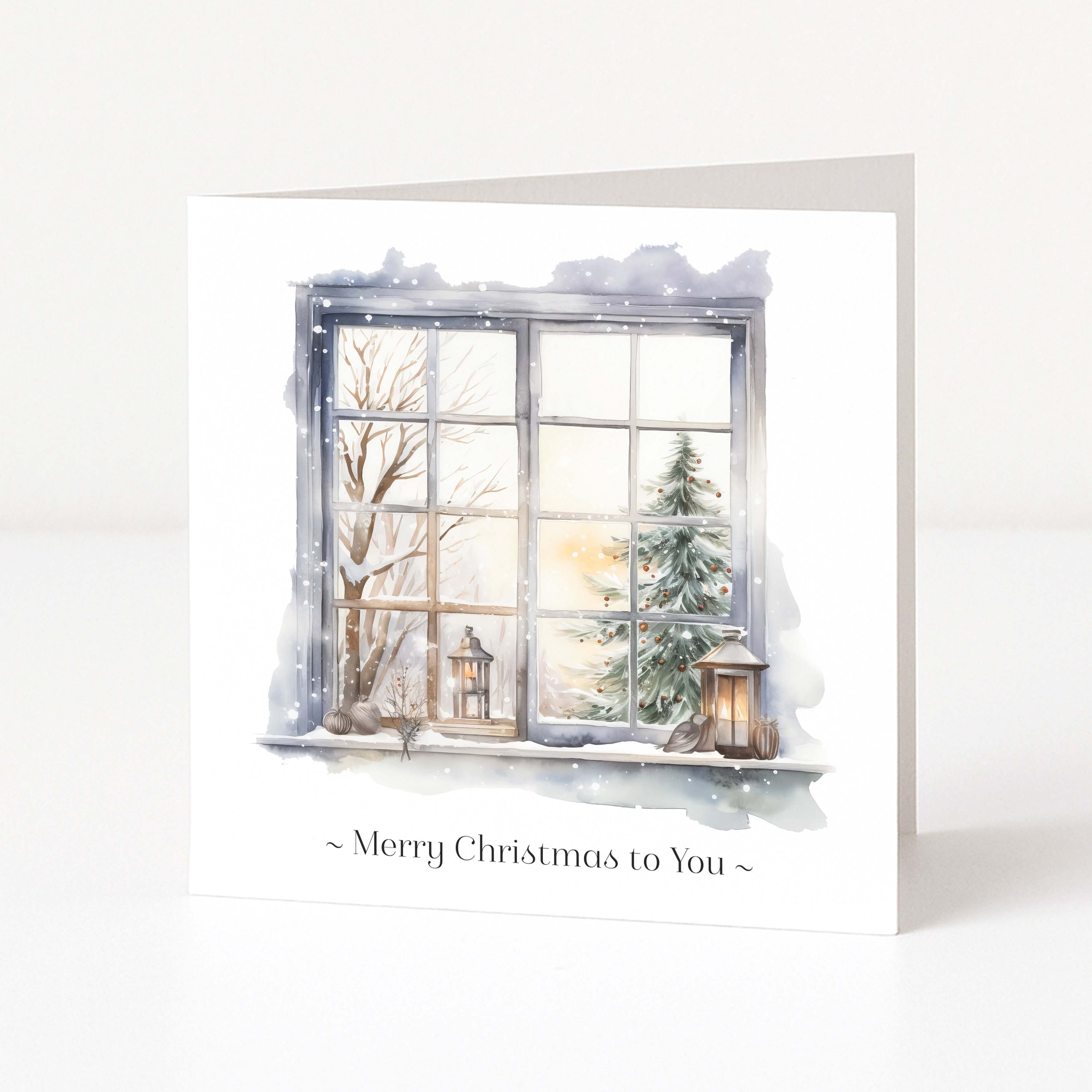 A square white Christmas greeting card standing upright on a white surface. The front features an illustrated snowy window scene with bare trees, a evergreen tree, lanterns, and the text '~ Merry Christmas to You ~' below the artwork.