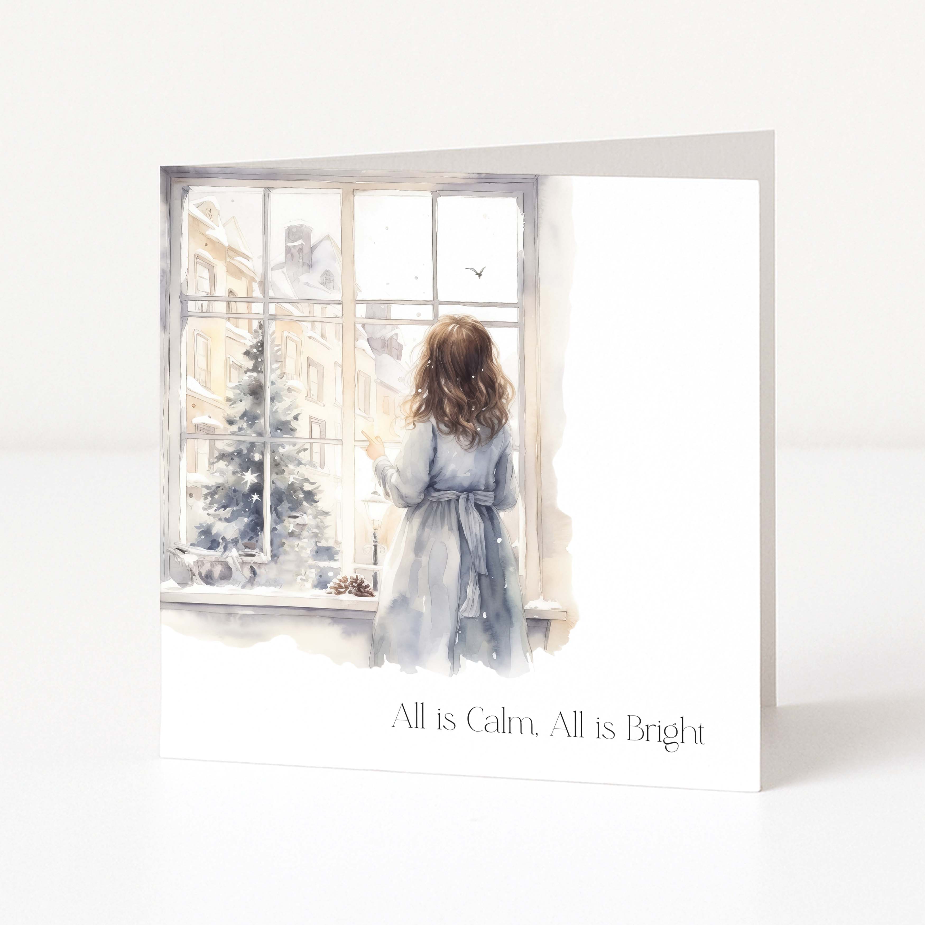 A square greeting card with a watercolor illustration of a girl looking out a window at a snowy tree, with the text 'All is Calm. All is Bright' at the bottom, shown standing on a white surface.