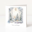 A white greeting card standing upright on a white surface, featuring an illustrated winter scene seen through an open window with snowy trees, wrapped gifts, and the text 'Merry and Bright' below.