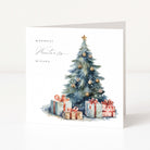 A square white Christmas card standing upright on a light surface, featuring a watercolour Christmas tree with ornaments and wrapped presents beneath, plus the text 'WARMEST Winter Wishes' in black script.