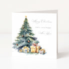 A square Christmas greeting card standing upright on a white surface. The card features a watercolor illustration of a decorated Christmas tree with wrapped gifts at the base and elegant script text reading 'Merry Christmas and a very happy New Year.