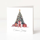 A square white Christmas greeting card standing upright on a white surface, featuring a watercolour-style Christmas tree with red ornaments, wrapped presents, and the script text 'Season's Greetings' at the bottom.
