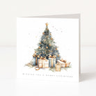 A square Christmas greeting card standing upright on a white surface. The front features a watercolor-style illustration of a decorated Christmas tree with gold ornaments, wrapped gifts, and the text 'WISHING YOU A MERRY CHRISTMAS' at the bottom.