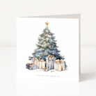 A square white Christmas greeting card standing upright on a light surface, featuring a watercolour-style Christmas tree with gold ornaments and several wrapped presents beneath it. The card reads 'JOY TO THE WORLD' at the bottom.