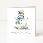 A square white Christmas greeting card standing upright, printed with a watercolor snowman wearing a gray top hat and blue scarf, with small greenery and red berries at the base and the text 'Wishing you a Merry Christmas' below.