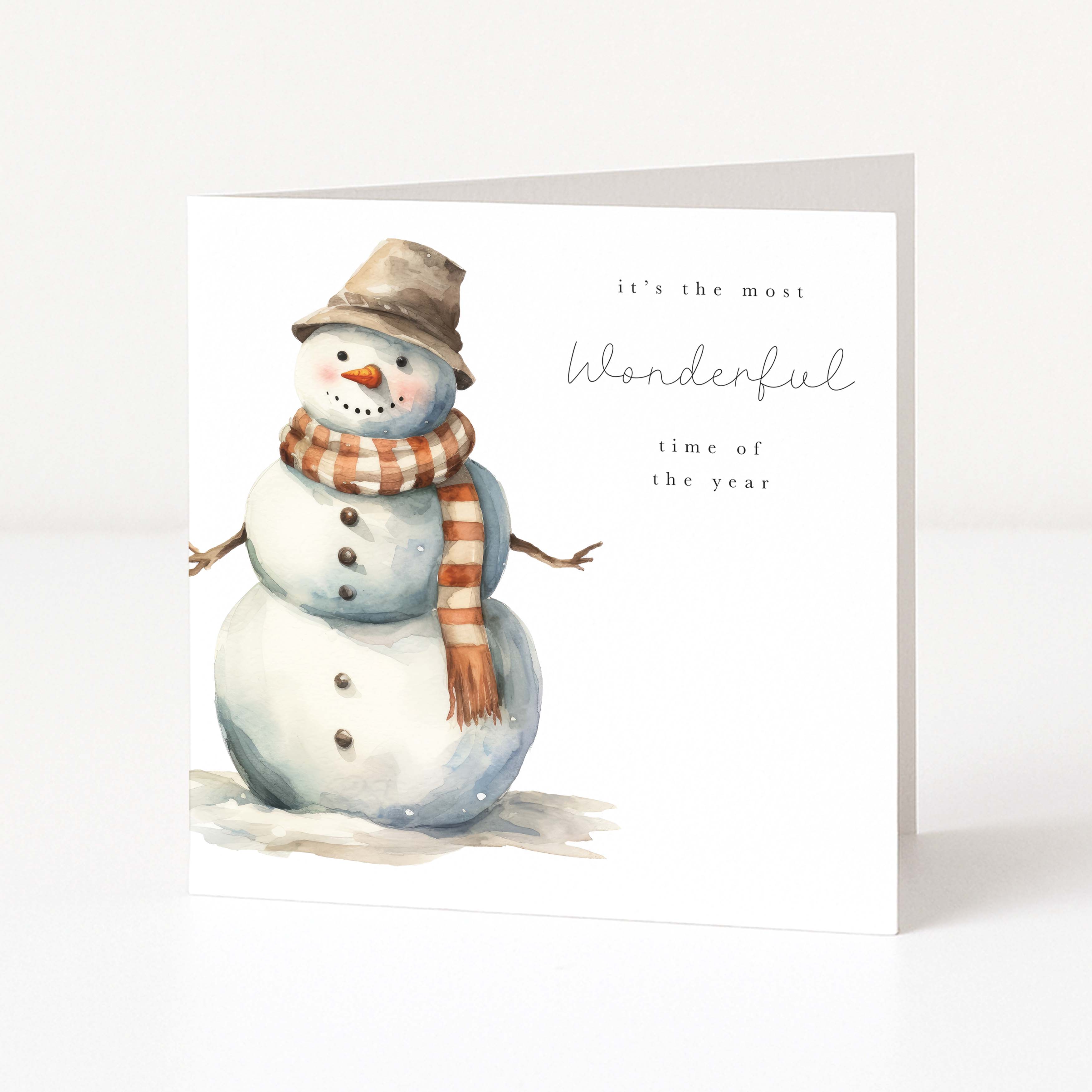 A square white Christmas greeting card featuring a watercolor snowman wearing a brown hat and an orange-and-white striped scarf, with the text 'it's the most Wonderful time of the year' on a clean white background.