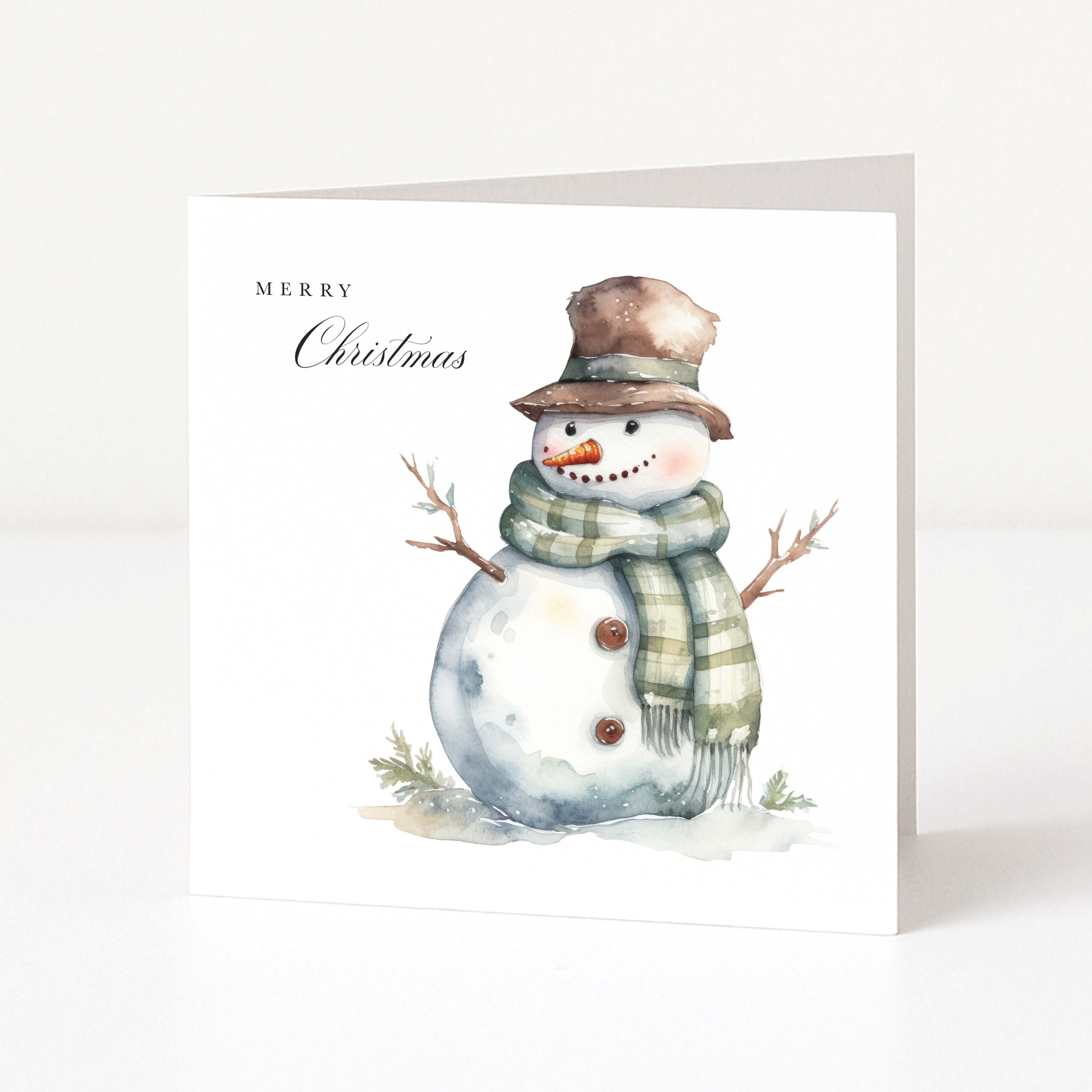 A square white Christmas greeting card standing upright, featuring a watercolor illustration of a snowman wearing a brown hat and a green-and-white striped scarf, with the text 'MERRY Christmas' printed on the left side.