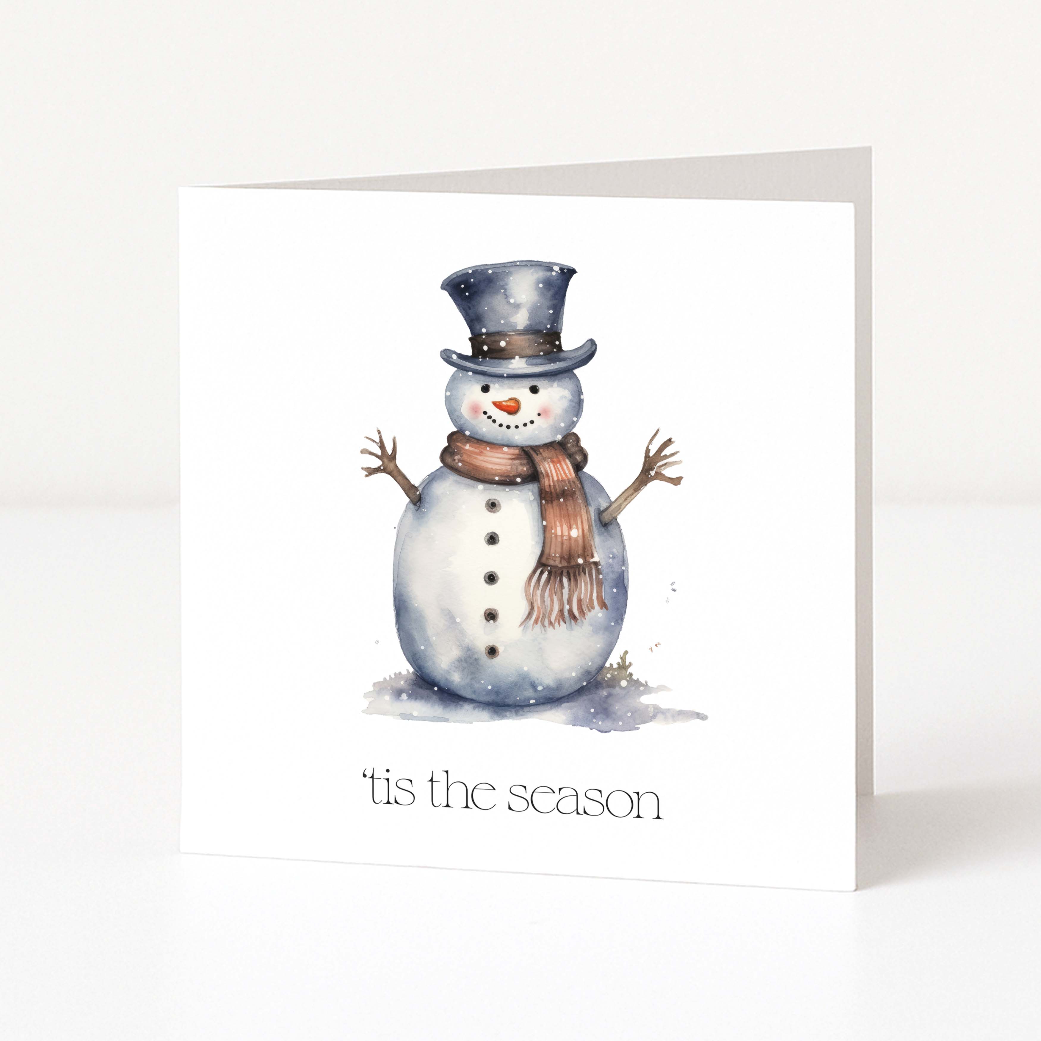 A white Christmas greeting card featuring a watercolour illustration of a snowman wearing a dark top hat and a brown scarf, with the text "tis the season" printed below.