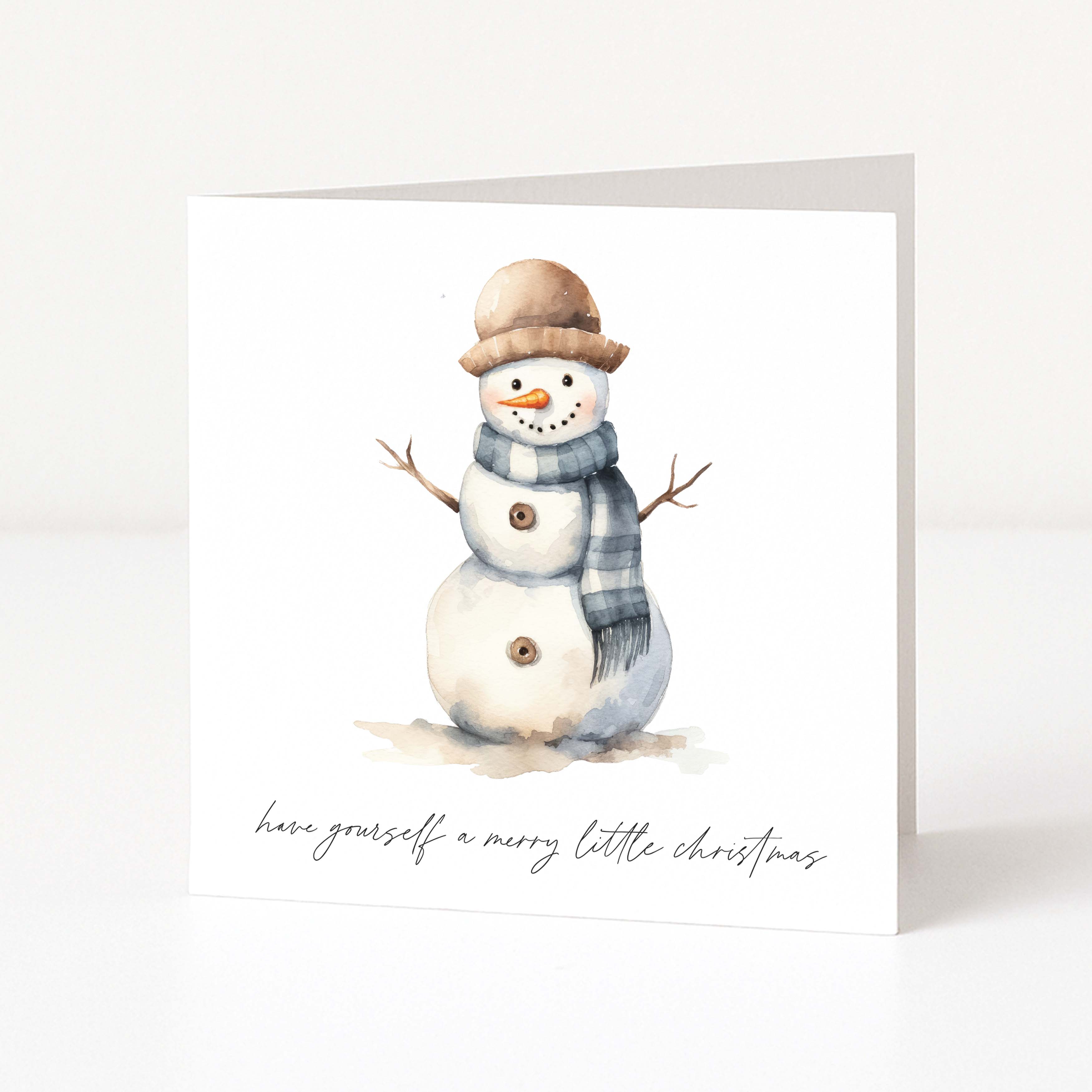 A square white Christmas greeting card standing upright on a white surface, printed with a watercolour snowman wearing a tan hat and blue-grey scarf, with the phrase 'have yourself a merry little christmas' in black script at the bottom.