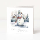 A square white Christmas greeting card standing upright, printed with a watercolour winter scene featuring a snowman wearing a grey top hat and red plaid scarf, with the text 'Season's Greetings' at the bottom.