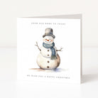 A square white Christmas greeting card standing upright on a light gray surface. The front features a watercolor-style snowman wearing a gray top hat and blue plaid scarf, with the text 'FROM OUR HOME TO YOURS' above and 'WE WISH YOU A HAPPY CHRISTMAS' below.