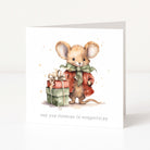 A square Christmas greeting card shown standing upright on a white surface. The card features a watercolour illustration of a small brown mouse wearing a red coat and green bow, standing next to a wrapped gift box.