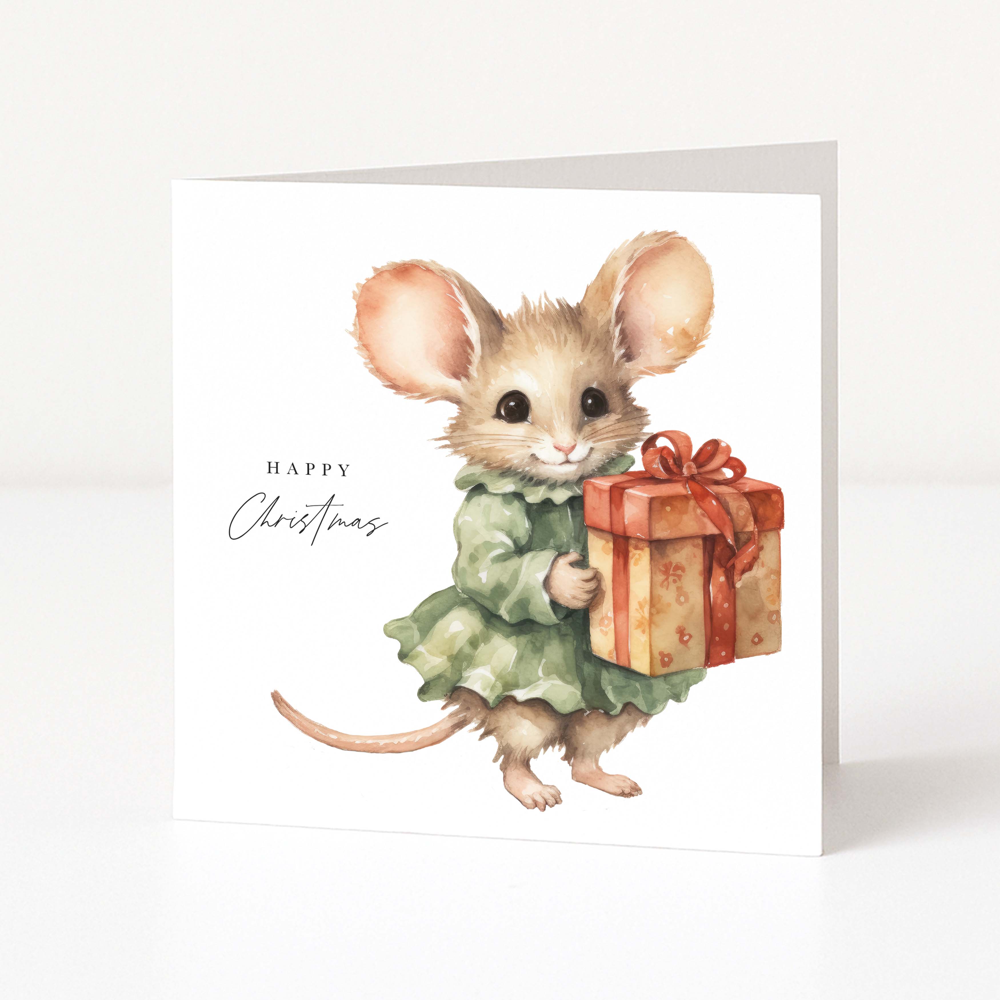 A square white Christmas greeting card featuring a watercolour illustration of a small mouse in a green dress holding a wrapped gift box, with the text 'Happy Christmas' on the left.